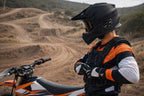 Person in motocross gear standing next to a dirt bike on a trail