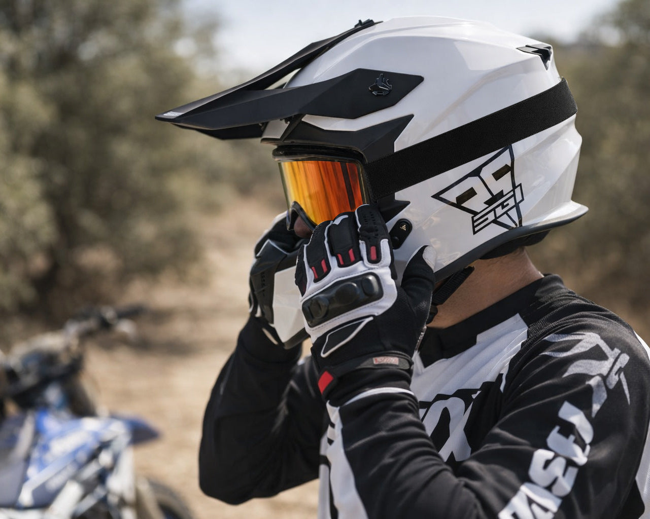 Person wearing a white and black helmet with orange visor, standing in a natural setting.